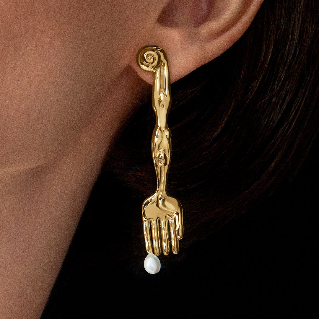 Modelo usando brinco em prata 925 com banho de ouro 18k de garfo com corpo surrealista e pérola natural