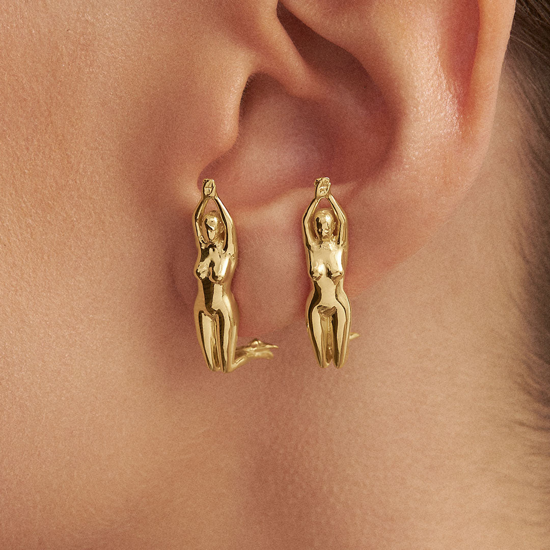 Modelo com brincos de esculturas de mulheres em prata 925 e banho em ouro 18k