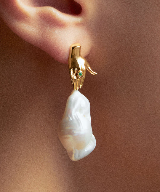 Modelo usando brinco de mão em prata 925 com banho de ouro 18k, esmeralda e pérola barroca