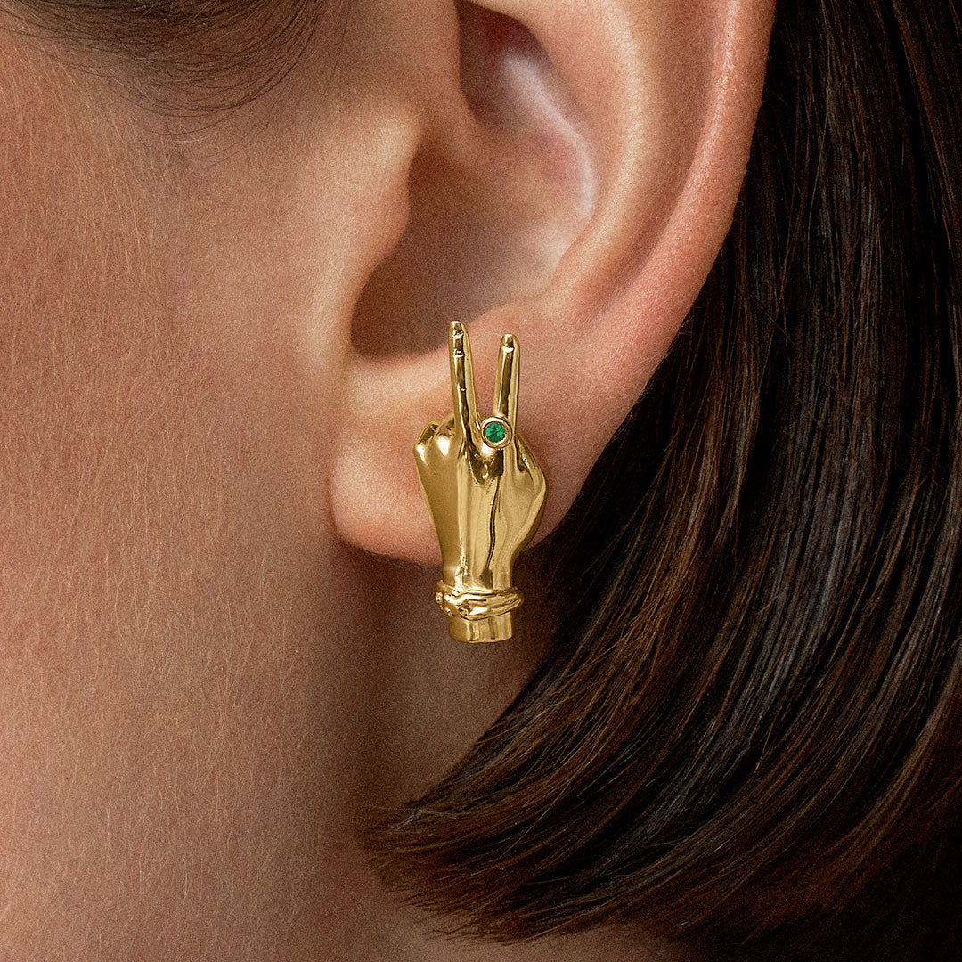 Modelo usando brinco de mão com sinal de paz em prata 925 com banho de ouro 18k e esmeralda