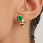 Modelo usando brinco em ouro 18k de mão segurando esmeralda retangular