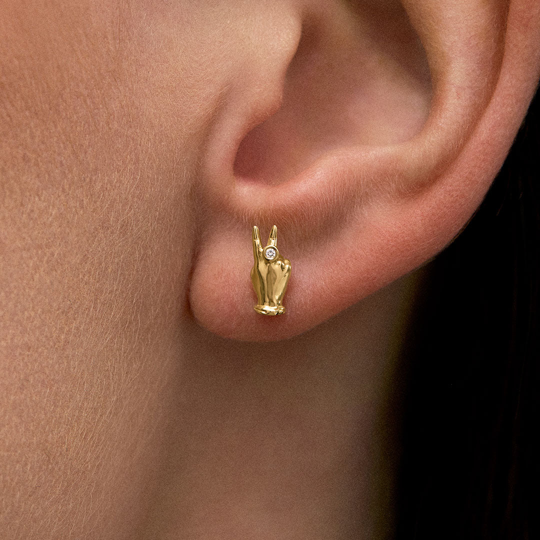 Modelo usando brinco em ouro 18k de mini mão em sinal de paz com diamante