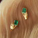 Brincos de ouro 18k de mãos segurando esmeralda retangular