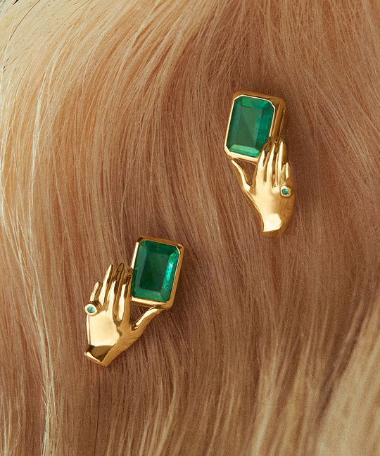 Brincos de ouro 18k de mãos segurando esmeralda retangular