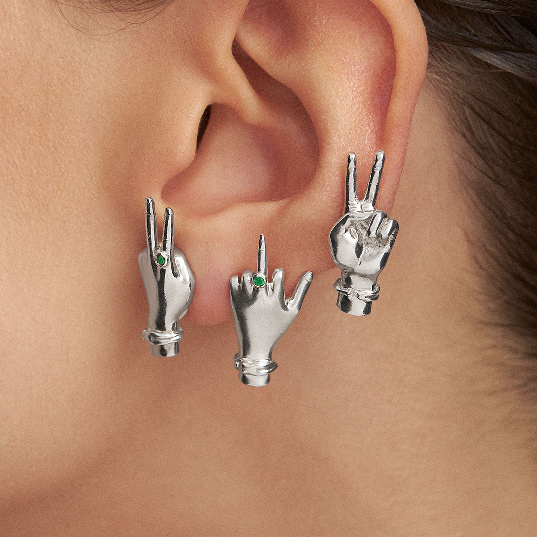 Modelo usando brincos de prata 925 e esmeraldas de mãos fazendo sinais