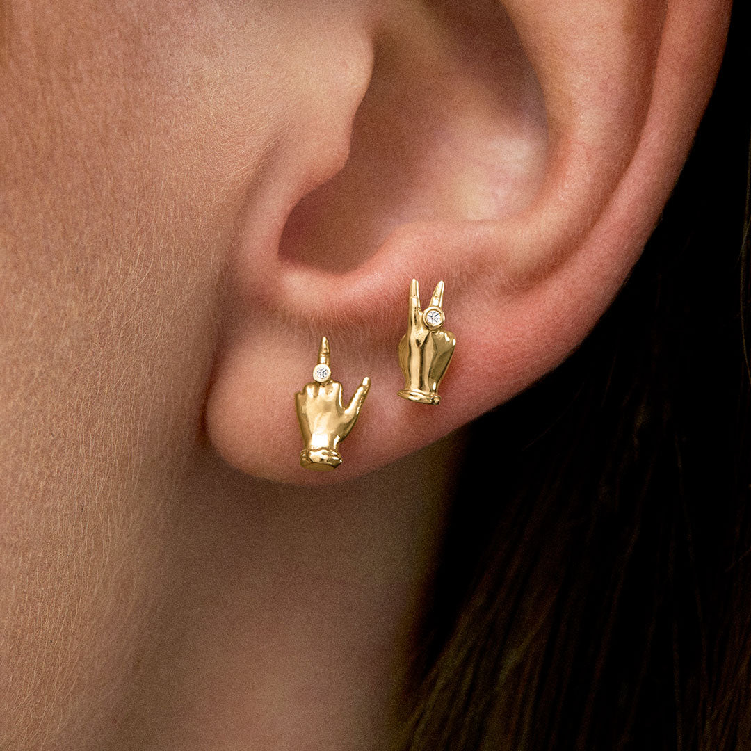 Modelo usando brincos em ouro 18k de mini mão em sinal de paz e dedo do meio com diamantes