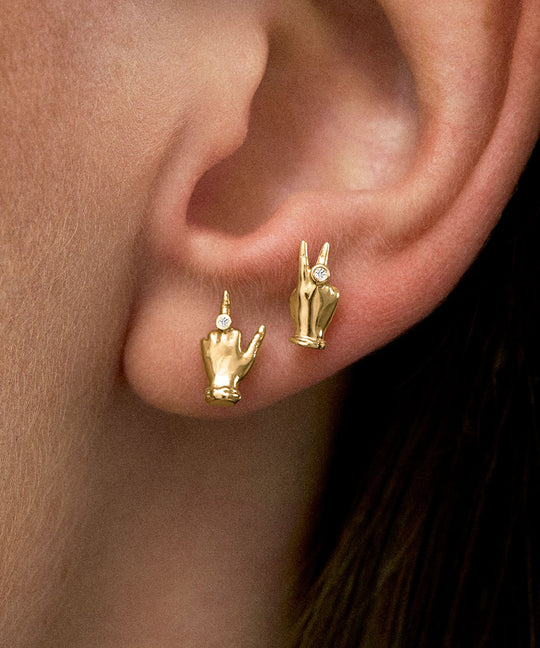 Modelo usando brincos em ouro 18k de mini mão em sinal de paz e dedo do meio com diamantes
