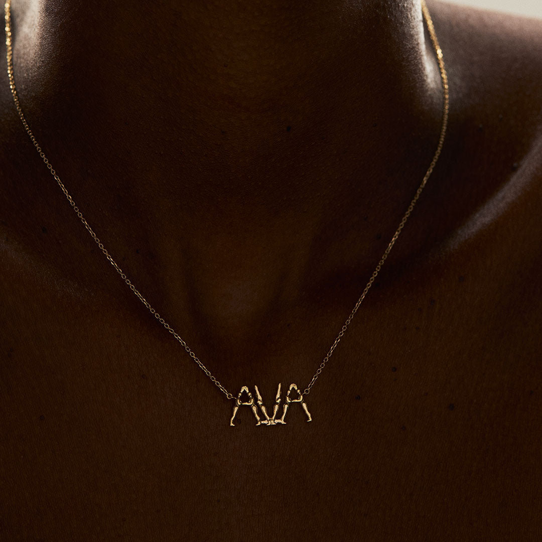Modelo usando colar em ouro 18k personalizável de nome com letras em forma de corpos femininos